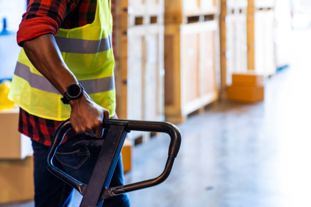 Close up of african black warehouse worker hand hold hand pallet jack in distribution warehouse with copyspace. Business warehouse and logistic concept.